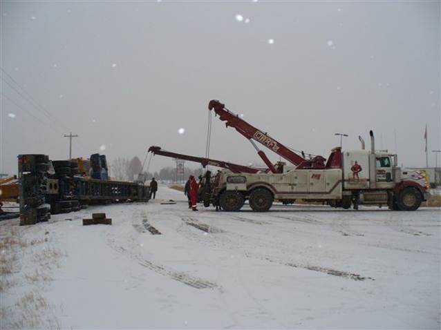 Truck with rig rolled over on the road, with a crane preparing to lift it.